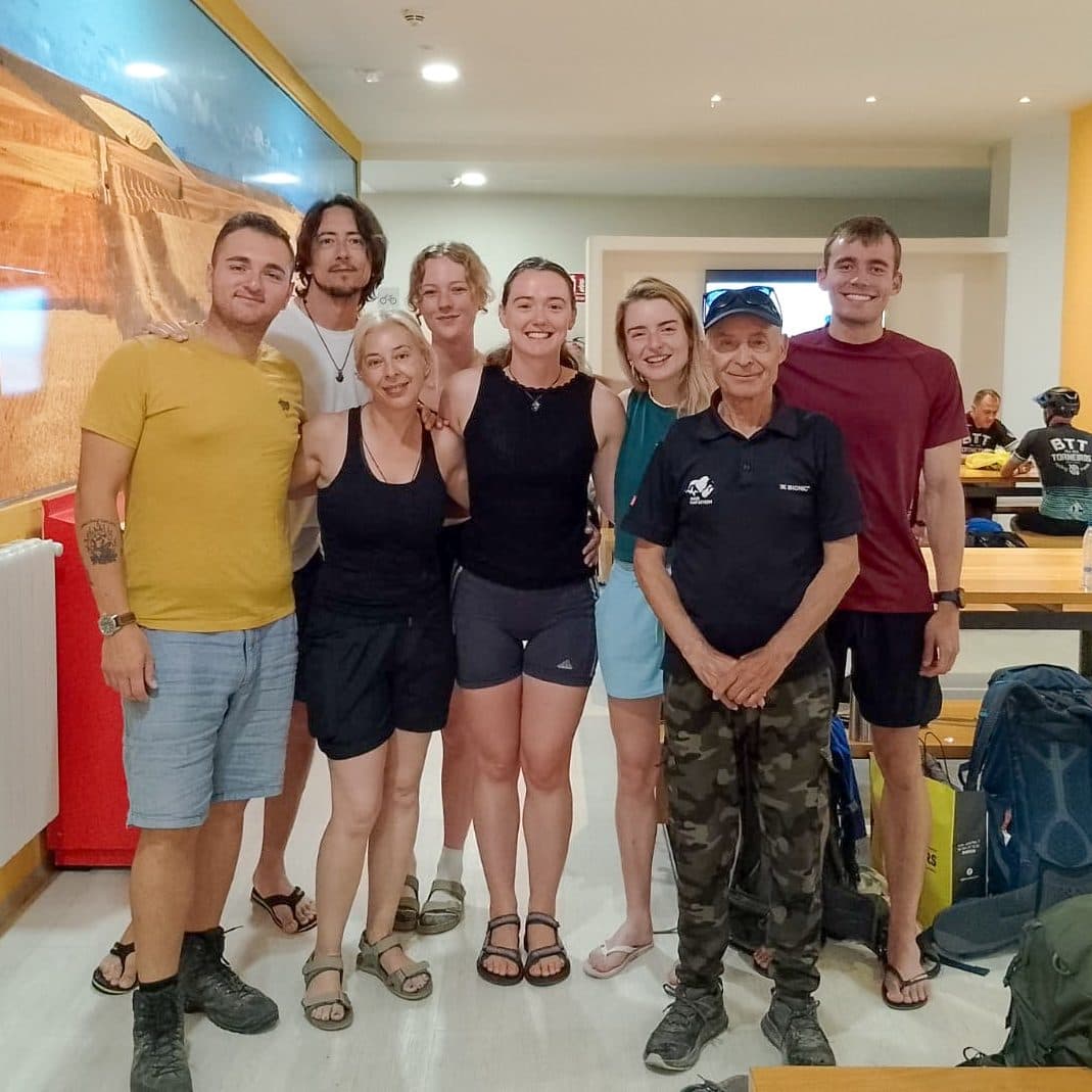 Pilgrims lined up smiling with their hospitalero inside an albergue.