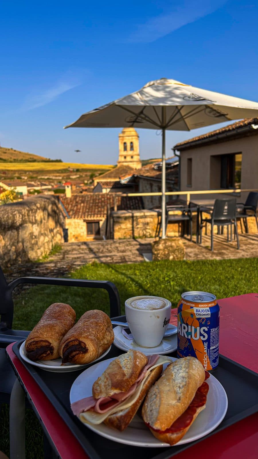 Bocadillos and café con leche on a terrace table, a Spanish church tower behind.