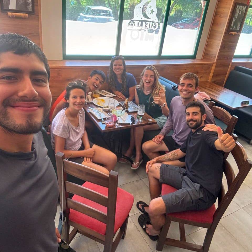 Six pilgrims crowded around a café table, grinning at the camera.