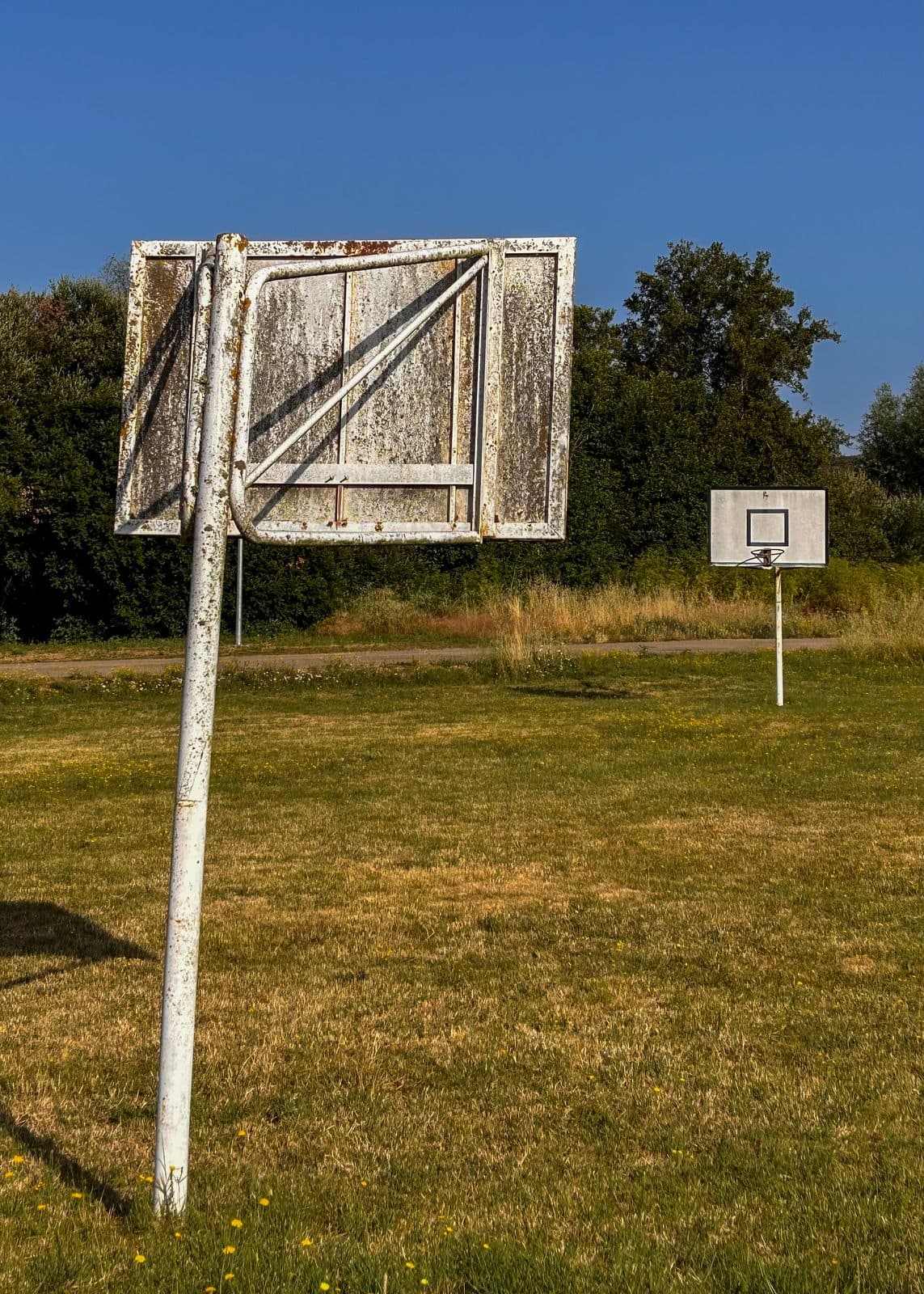 Weathered wooden basketball backboards standing in a grassy village field.