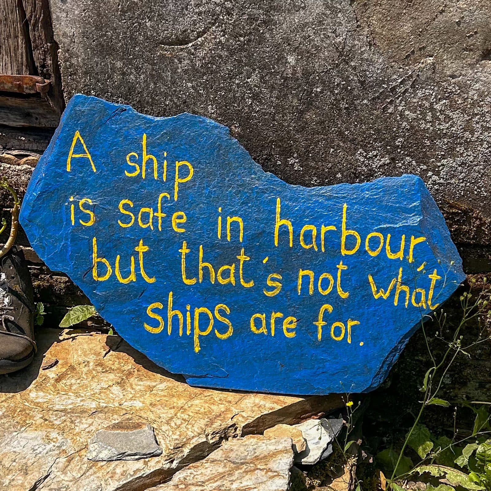 A blue-painted trail stone reading: a ship is safe in harbour, but that's not what ships are for.
