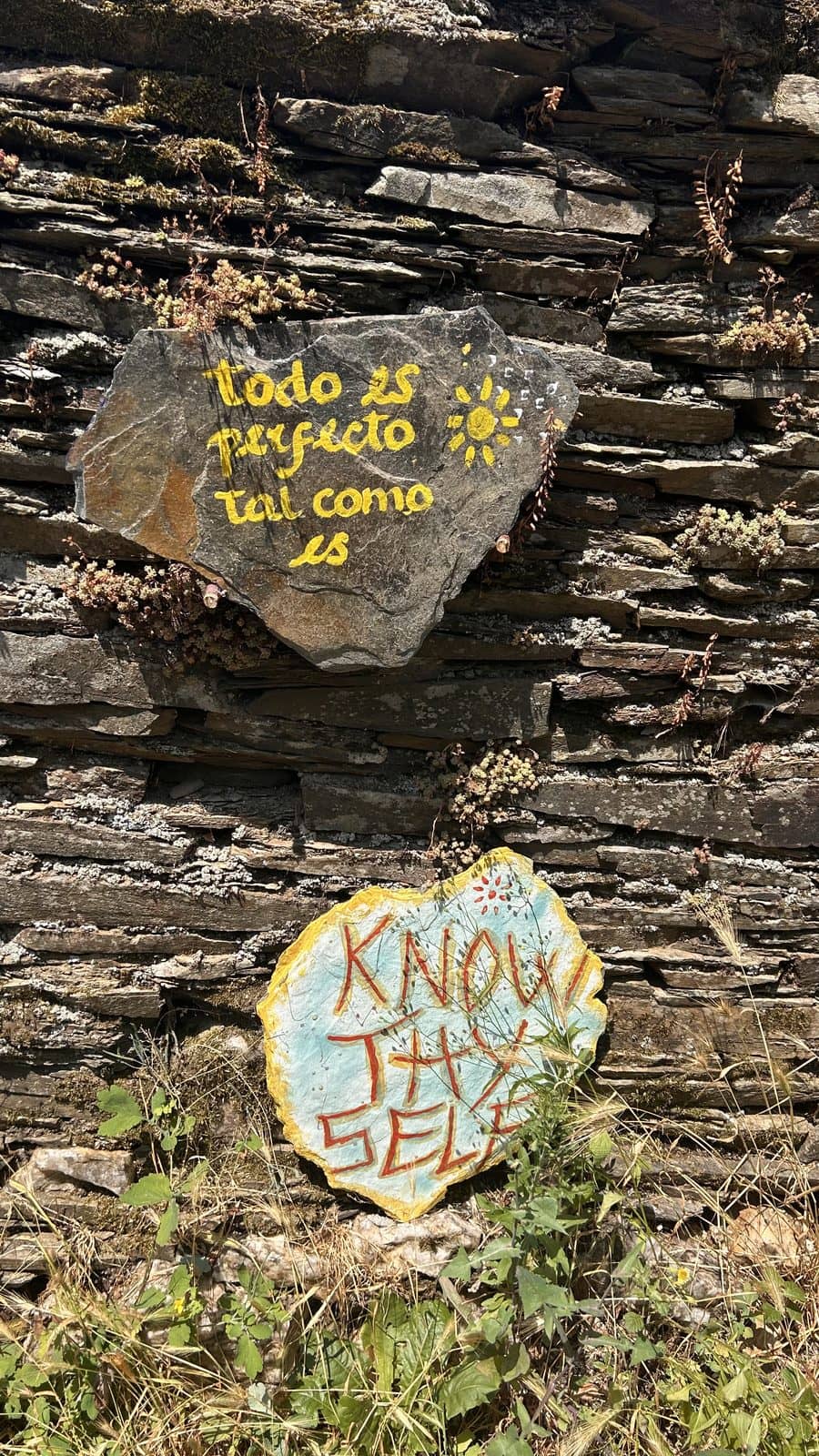 Painted stones tucked into a Galician slate wall reading Know Thyself and todo es perfecto tal como es.