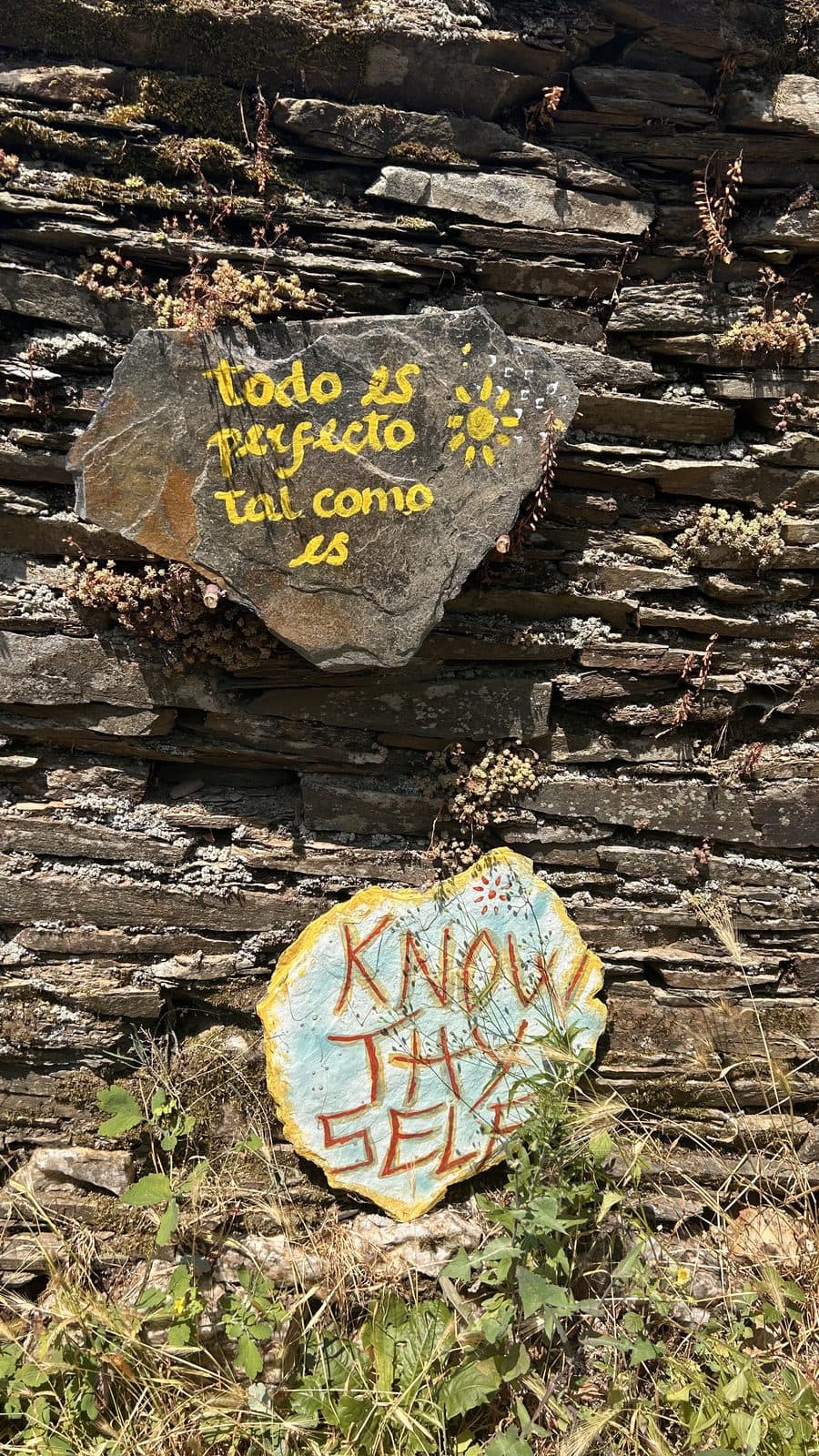Painted stones tucked into a Galician slate wall reading Know Thyself and todo es perfecto tal como es.