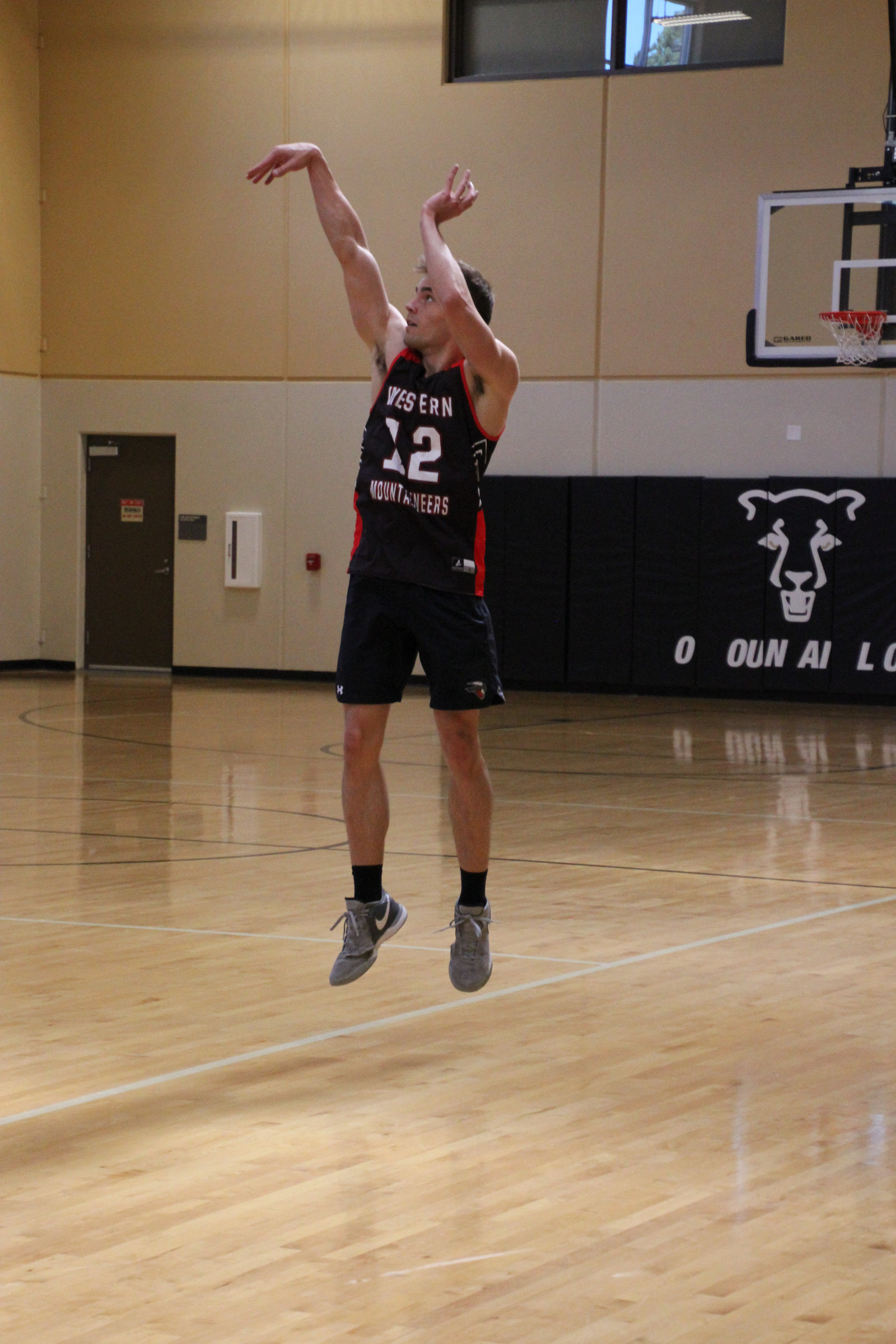 Kyle Wisniewski in a black Western Mountaineers jersey, number 12, in the air on a jump shot in an indoor gym.