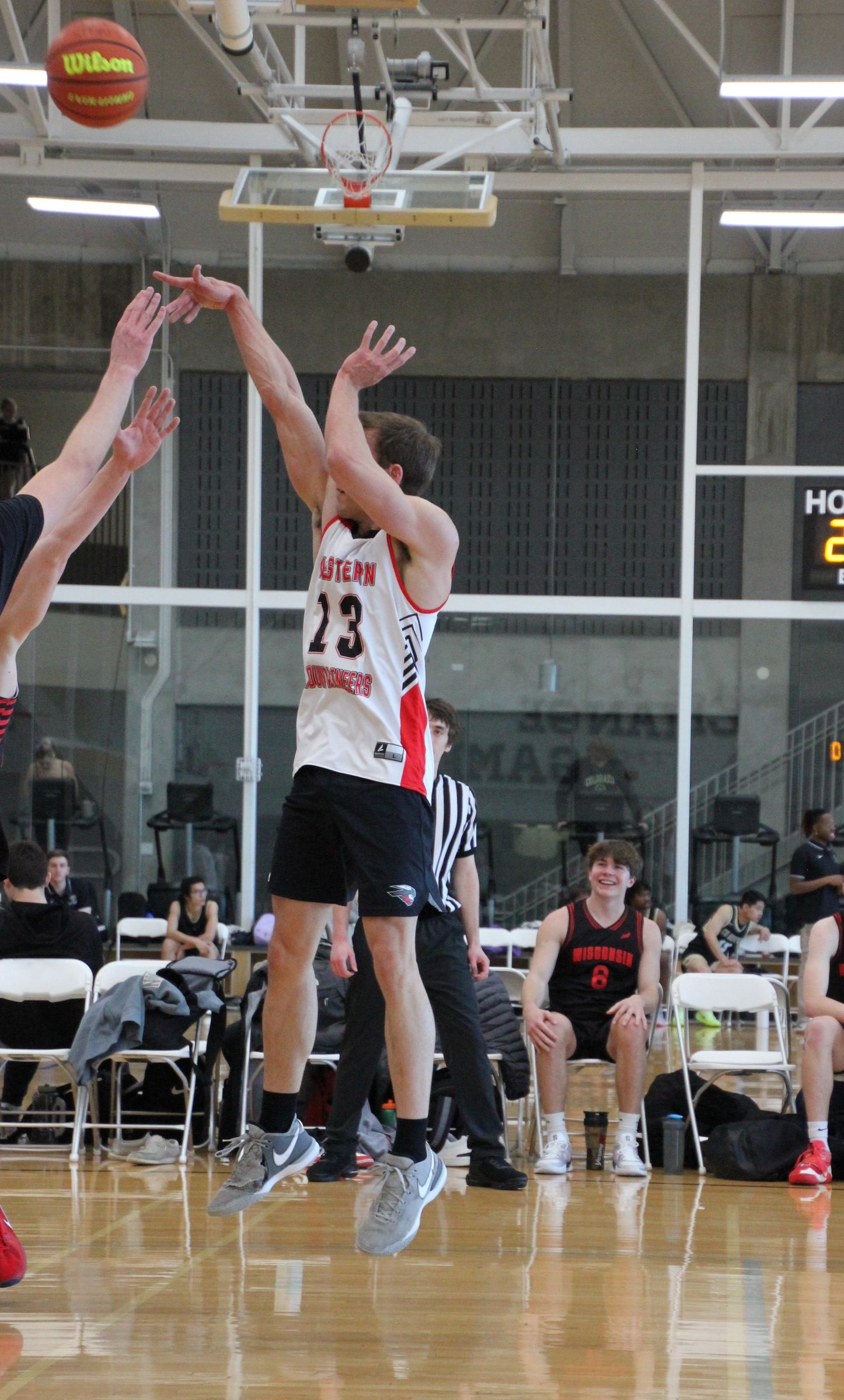 Kyle Wisniewski in a white Western Mountaineers jersey, number 13, releasing a jump shot as a defender’s hands reach in from the left, the ball high above.