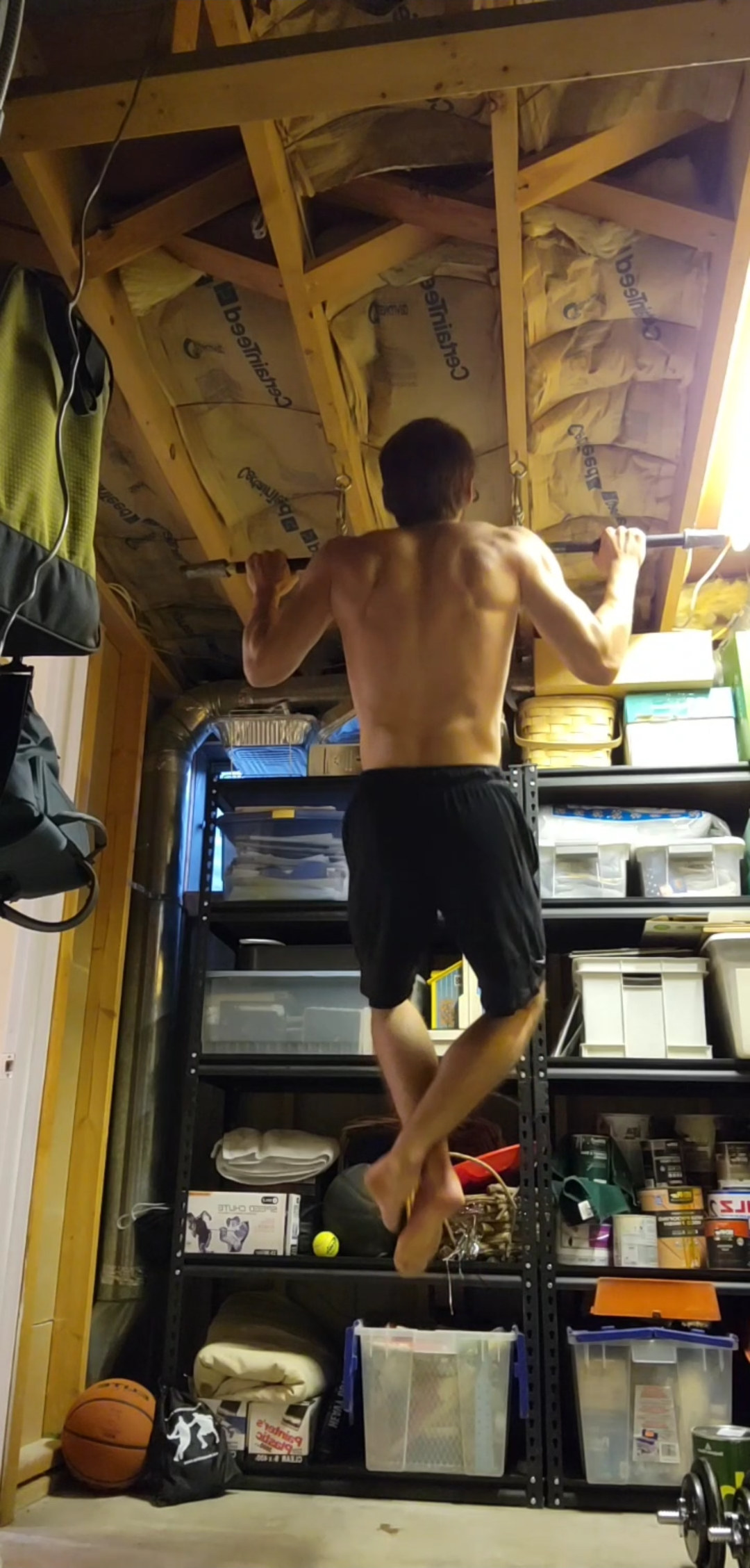 Kyle Wisniewski from behind, mid pull-up on a bar fixed under exposed ceiling joists.