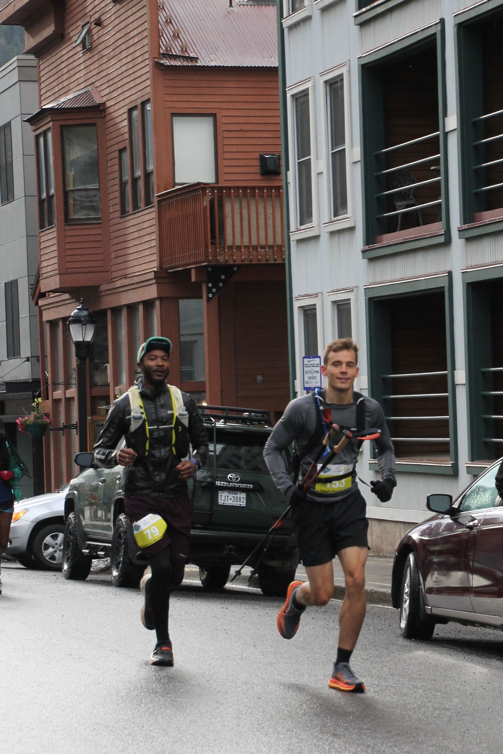 Kyle Wisniewski running beside another runner past parked cars on a Telluride street.