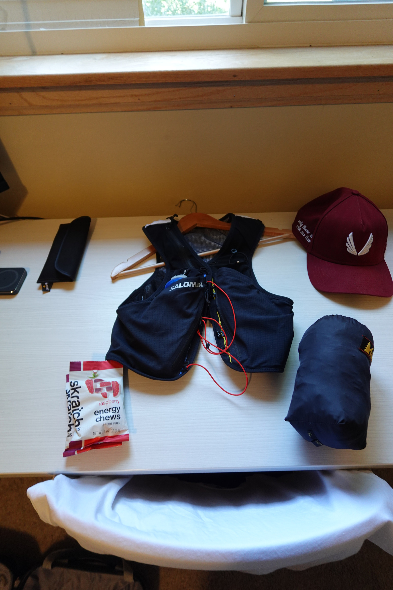 A race vest, red cap, energy chews and a rolled jacket laid out on a desk.